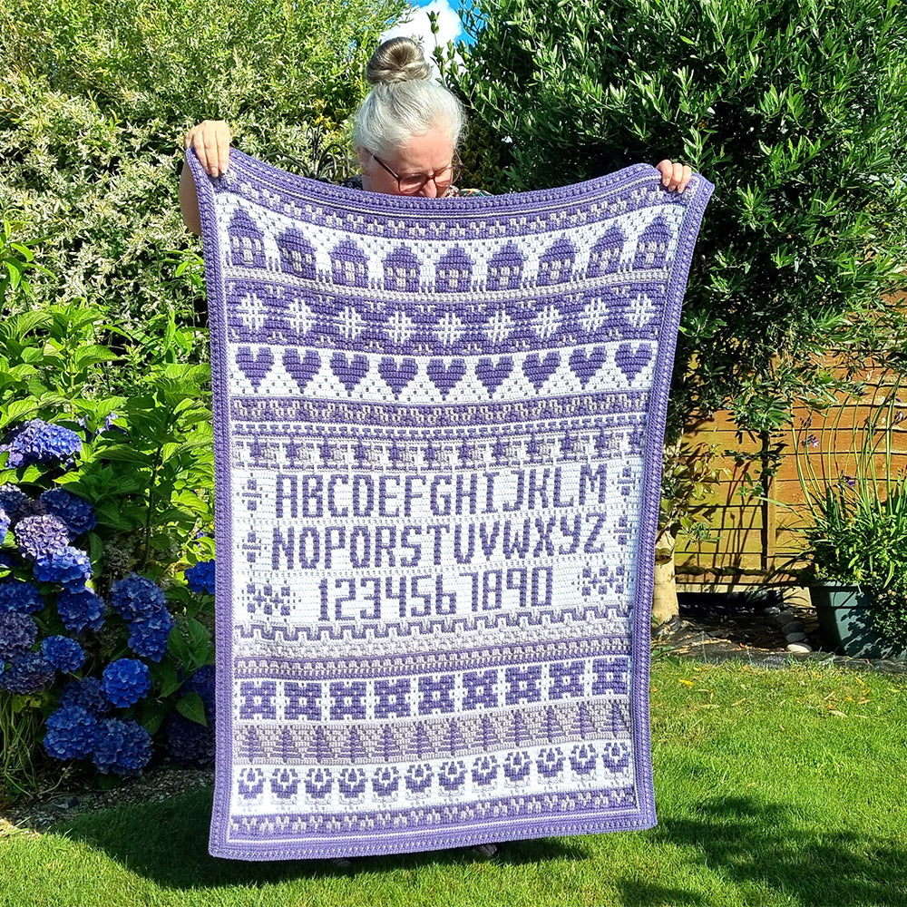 Rosina Plane Lakenham Mosaic Sampler CAL Haakpakket - Ultra Violet deken in lila- en paarstinten vastgehouden in de tuin