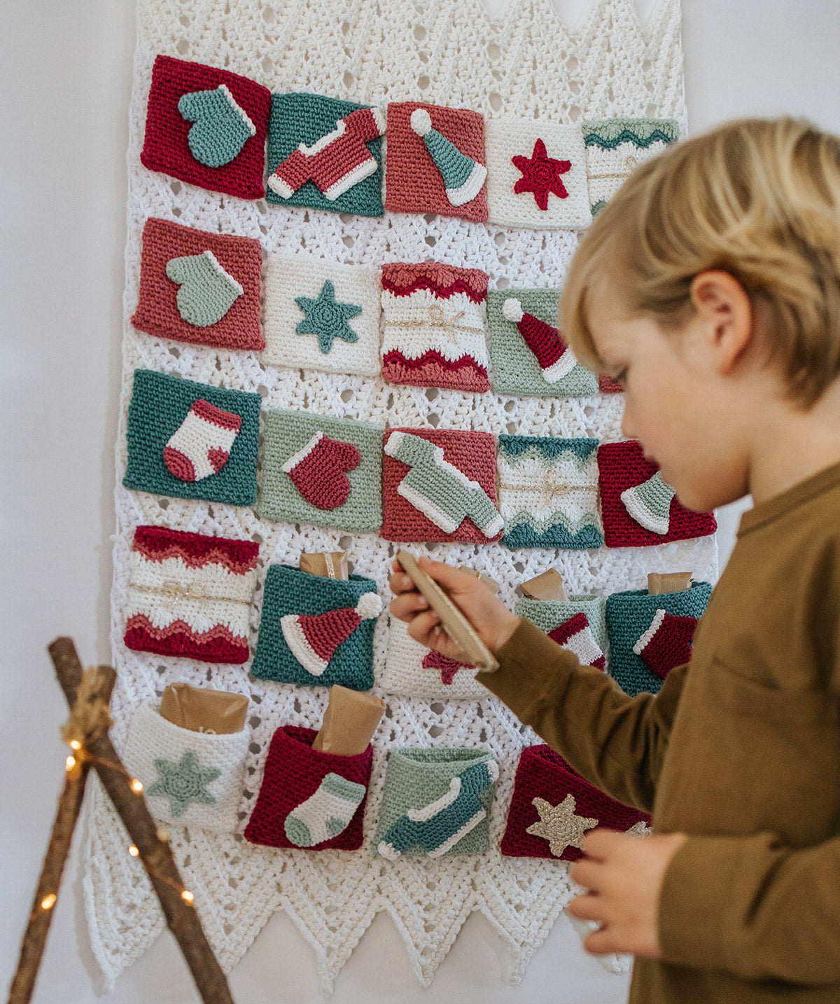Gehaakte Durable Adventskalender met 24 kerstzakjes en kind dat een cadeautje uit de kalender haalt